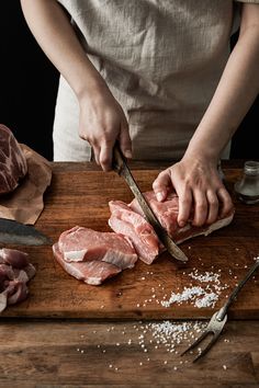 a person cutting meat on top of a wooden cutting board next to utensils