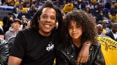 two people sitting next to each other in front of a crowd at a basketball game