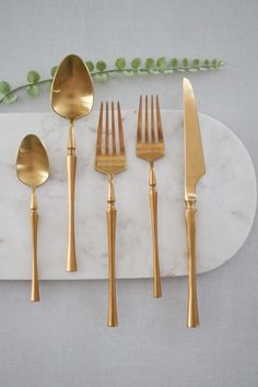 five gold flatware forks and spoons on a marble platter