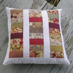 a decorative pillow made with patchwork and white linens sitting on a wooden deck