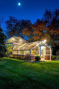 a lit up greenhouse at night in the middle of a field with trees and grass