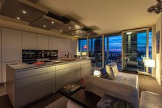 a living room filled with furniture and a large window overlooking the cityscape at night