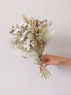 a person holding a bouquet of flowers in their hand on a white wall with no one around it