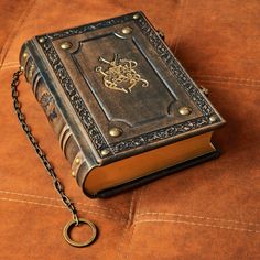 an old book with a chain attached to it sitting on a brown leather couch next to a key