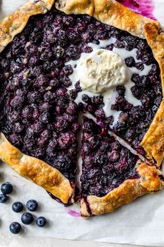 a pie with blueberries on it sitting on top of a piece of parchment paper