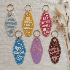 six keychains with different designs on them sitting next to some dried plants and flowers