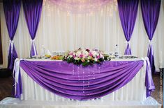 a table with purple drapes and flowers on it is set up for a wedding reception