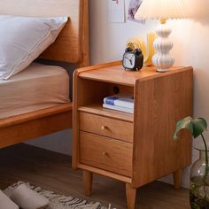 a nightstand with a clock on it next to a bed