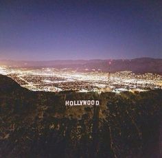 the hollywood sign is lit up at night on top of a hill with city lights in the background