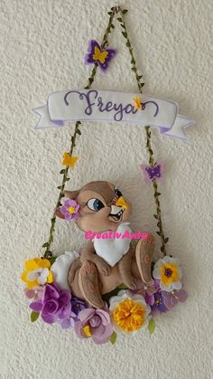 a stuffed animal hanging from the side of a wall with flowers and butterflies around it