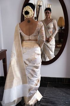 a woman standing in front of a mirror wearing a white sari with flowers on it