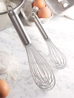 two metal whisk attachments sitting next to eggs