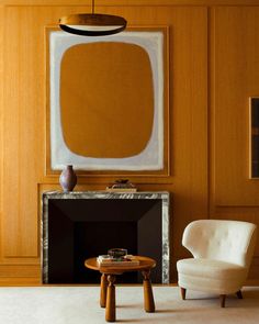 a chair and table in front of a fireplace with a painting on the wall behind it