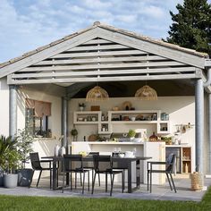 an outdoor kitchen and dining area is shown in this backyard setting with grass, shrubs, and potted plants