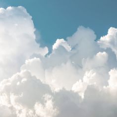 the plane is flying high in the sky with many clouds behind it and blue skies above