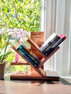 a stack of books sitting on top of a wooden stand next to a window sill