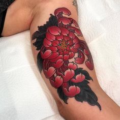 a person with a tattoo on their arm that has red flowers and leaves around it