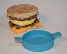 a hamburger with egg and cheese on it next to a blue bowl