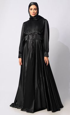 Introducing our exquisite Lycra Satin Flared Abaya, a stunning fusion of elegance and contemporary style. Crafted with meticulous attention to detail, this abaya is designed to elevate your modest fashion wardrobe to new heights. The flared silhouette adds a touch of graceful movement, enhancing the overall allure of the garment. Featuring a front draped pleated style, which adds texture and dimension, creating visual interest and a unique focal point. Complementing the pleats are satin show buttons, delicately embellishing the front of the abaya for a refined finish. For added versatility and cinched-in definition, an attached belt accompanies the abaya, allowing you to adjust the fit according to your preference and accentuate your waistline. The back zipper closure ensures a seamless an Formal Fitted Black Abaya, Elegant Black Abaya With Modesty Panel, Elegant Black Abaya For Formal Occasions, Elegant Black Formal Abaya, Black Formal Gown For Eid, Black Satin Gown With Long Sleeves, Elegant Fitted Black Abaya, Traditional Long Sleeve Satin Dress, Satin Floor-length Abaya For Eid