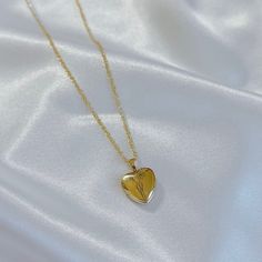 a gold heart shaped necklace on a white satin background with the word love written in cursive writing