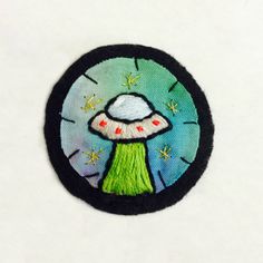 an embroidered patch with a green mushroom on it's side and stars in the background