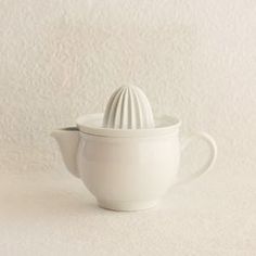 a white ceramic tea pot with a lid on the side and a strainer in the middle