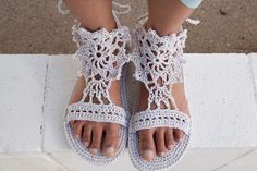 a woman's feet wearing white crocheted sandals on top of a sidewalk