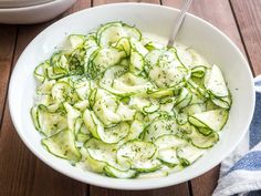 a white bowl filled with cucumbers and sauce on top of a wooden table