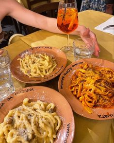 three plates of pasta and wine on a table with two people holding their hands over them