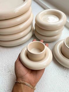 a hand holding a stack of cream colored dishes