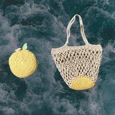 two crocheted purses sitting next to each other on the water with an orange