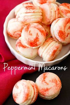 a white bowl filled with red peppermint macarons on top of a table