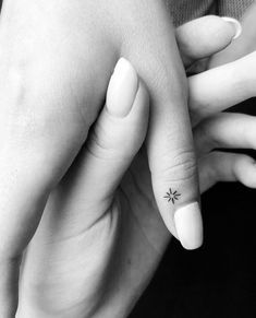 two hands holding each other with small tattoos on their fingers and one has a star tattoo on the middle finger