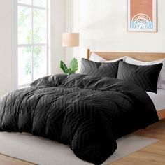 a bed with black comforter and pillows in a white room next to a window