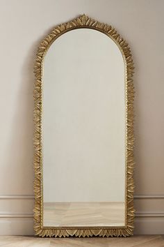 a large gold mirror sitting on top of a wooden floor next to a white wall