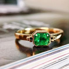 an emerald colored ring sitting on top of a stack of magazines with the lid open