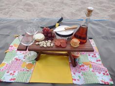 a picnic table set up on the beach with wine, cheese and crackers next to it