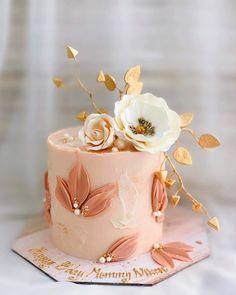 a pink cake with white flowers and gold leaves on top, sitting on a table