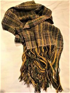 This is a warm, soft wool scarf with curvy edges in green, brown, gold and beige, and finished with a long fringe.  It is textured and there is a slight sparkle which lifts the colours and gives it a luxurious feel.  The colours are rustic woodland colours, perfect for the autumn or winter season. This was woven on a rigid heddle loom to my own design.  My primary interest is colour and yarn rather than complex patterns.  My work is almost exclusively natural fibres and therefore occasional smal Brown Handwoven Winter Scarves, Handwoven Brown Scarves For Fall, Rustic Clothes, Handmade Wool Scarf, Rigid Heddle Loom, Complex Patterns, Edge Scarf, Heddle Loom, Long Fringe