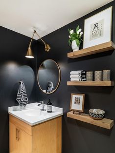 a bathroom with black walls and white counter tops, wooden shelves and a round mirror on the wall