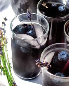 three glasses filled with ice and blueberries on top of a white table next to flowers