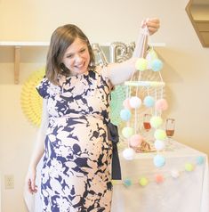 a pregnant woman holding up a mobile with pom poms hanging from it's sides