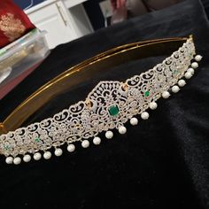 a tiara with pearls and emeralds on it sitting on a black velvet surface