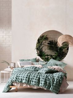 a bed with green comforter and pillows in front of a round mirror on the wall