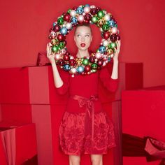 a woman in a red dress holding a christmas wreath over her head with balls on it