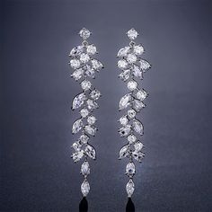 two pairs of diamond earrings on a black surface with the background showing dark gray ground