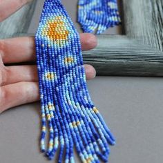 a hand holding a blue beaded brooch with yellow and white designs on it