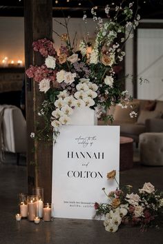 a sign with flowers and candles sitting on the ground in front of some couches