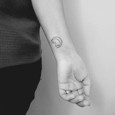 a woman's arm with a small wave tattoo on her left hand and the moon behind it