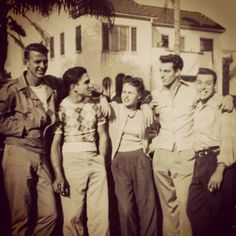 an old black and white photo of people standing in front of a house with their arms around each other